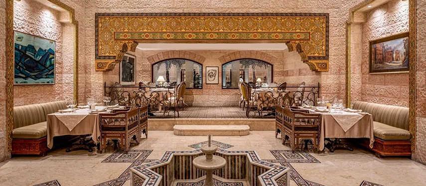 An atmospheric restaurant at Mövenpick Hotel Petra blends traditional décor, patterned floors and intimate dining tables set within arched stone interiors.