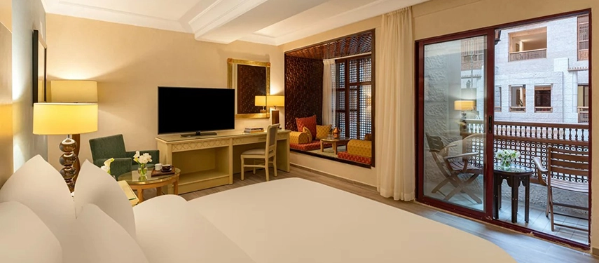 A spacious guest room at Mövenpick Hotel Petra features warm neutral tones, a comfortable seating area and doors opening onto a private terrace.