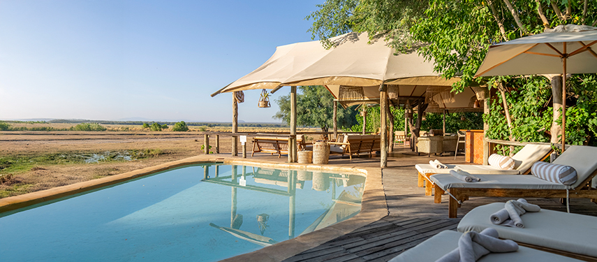 A serene pool deck at Anabezi overlooks the floodplain, shaded by canvas awnings and surrounded by loungers.