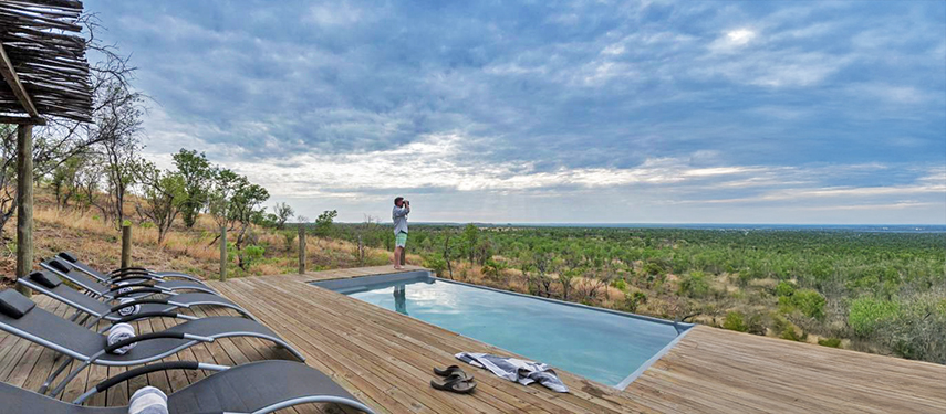 Man looks over the African grasslands standing next to a swimming pool in Zimbabwe
