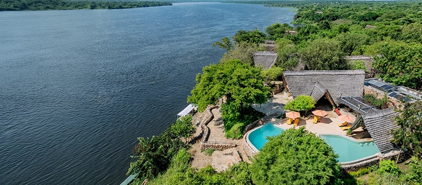 The main lodge and swimming pool sit above the Victoria Nile, surrounded by dense woodland and expansive river views within Murchison Falls National Park.