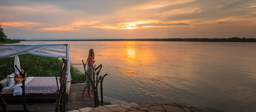 A peaceful sunset scene along the Victoria Nile, where a private deck and daybed overlook the glowing river as daylight fades.