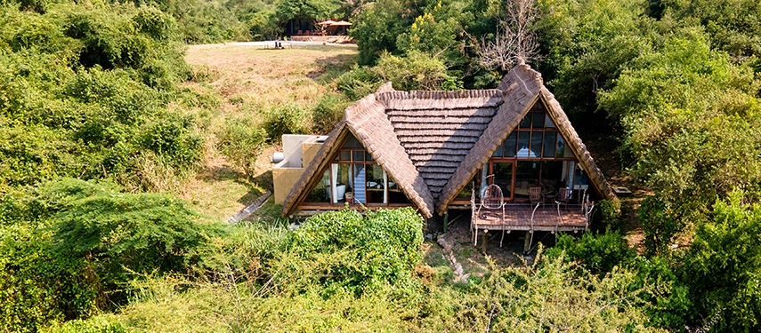 An aerial view of a private thatched suite tucked into dense greenery, with a deck overlooking the Victoria Nile.