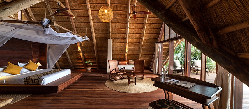 A refined safari suite interior with rocking chairs, woven rugs and floor-to-ceiling windows framing the surrounding forest.