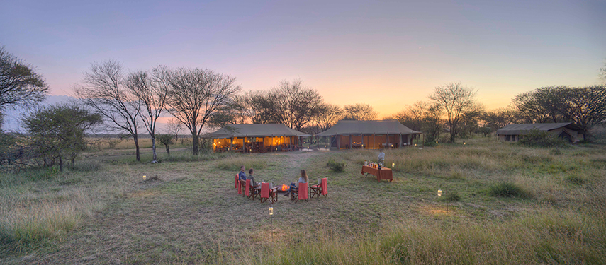 Guests enjoying sundowners around a firepit at Olakira Migration Camp as the sun sets.