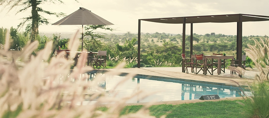 Peaceful poolside setting at Ololo Safari Lodge, with dining tables shaded by umbrellas and sweeping views of Nairobi National Park.
