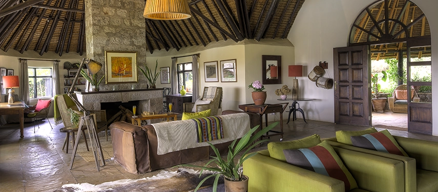Spacious guest lounge at Ololo Safari Lodge featuring stone walls, a large fireplace, and comfortable seating with vibrant African accents.