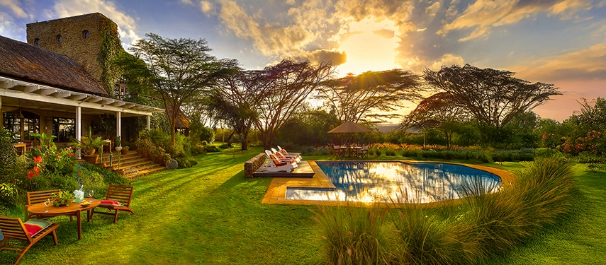 Golden light spilling across Ololo Safari Lodge’s gardens and pool, with acacia trees casting soft shadows in the tranquil dusk.
