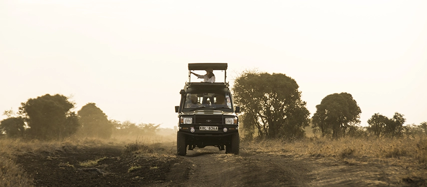 Safari vehicle driving through the savannah of Nairobi National Park in the golden light of dawn, ready for a morning game drive.