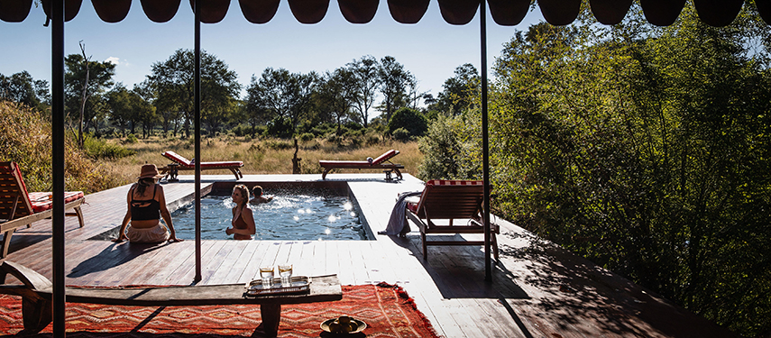 Guests relax by the pool deck at Mbamba Camp, surrounded by wilderness views.
