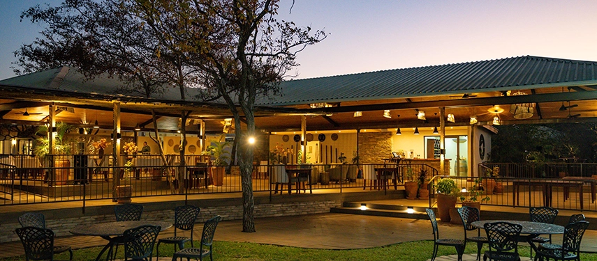 Open-air restaurant and bar terrace illuminated at dusk at Insika Lodge, Victoria Falls.
