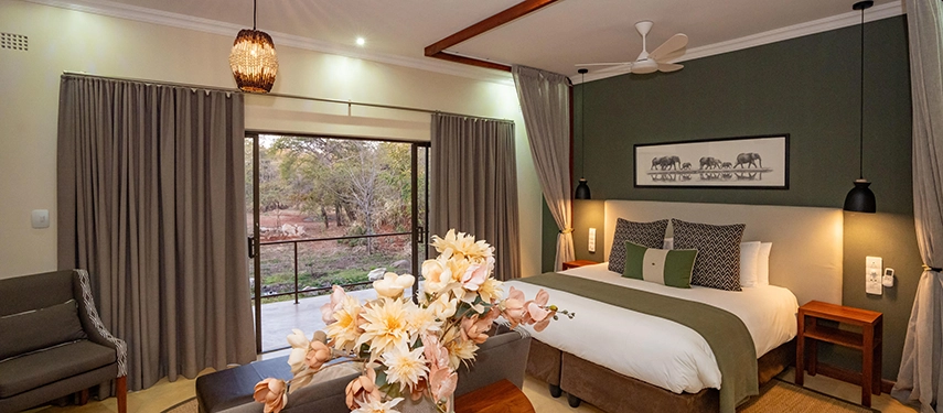 Signature suite with king bed, floral arrangement and views through sliding doors at Insika Lodge, Victoria Falls.