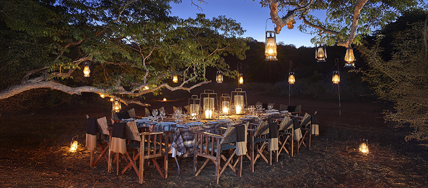 Al fresco dining table lit by lamps and candles in the bush in Zimbabwe