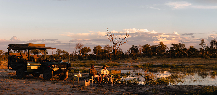 Guests enjoy sundowners by a waterhole after an afternoon game drive in the Okavango Delta.