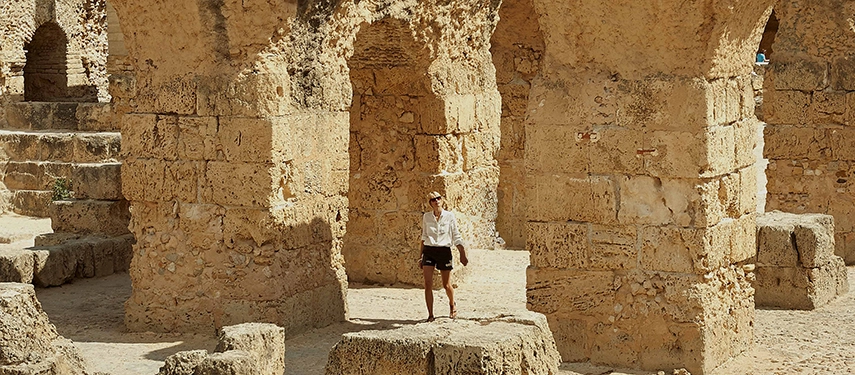 Traveller walking among the ancient sandstone arches of the Roman ruins of Carthage in Tunisia, bathed in golden light.