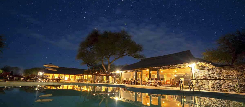 Poolside dining and lounge area at Tarangire Simba Lodge in Tanzania, lit up under a starlit sky.