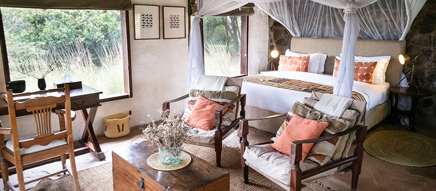 Elegant cottage interior featuring warm textiles, handcrafted furniture, and a mosquito-draped bed overlooking the wild grasslands.