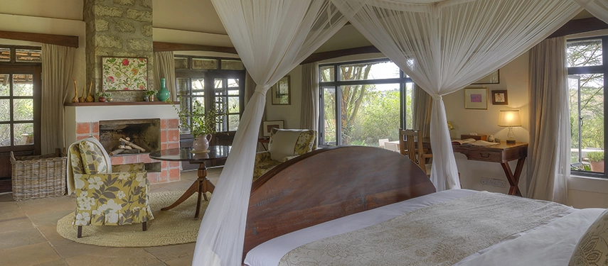 Bright and airy suite with canopy bed, sitting area, and glass doors opening to a private terrace overlooking Nairobi National Park.