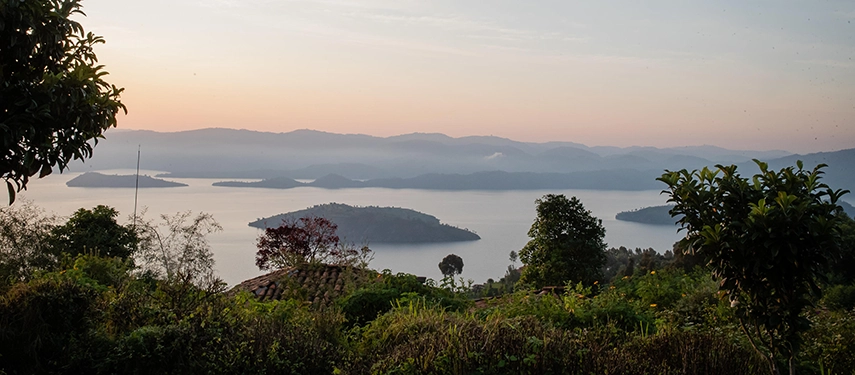The view from Virunga Lodge stretches across Lake Bulera at sunset, with islands scattered across the water and distant hills fading into soft evening light.