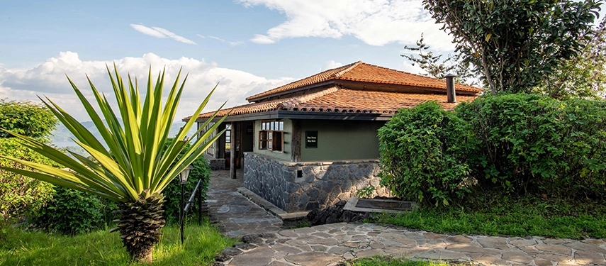 A stone cottage at Virunga Lodge sits along a garden-lined path, blending natural materials with sweeping views of Rwanda’s volcanic highlands.