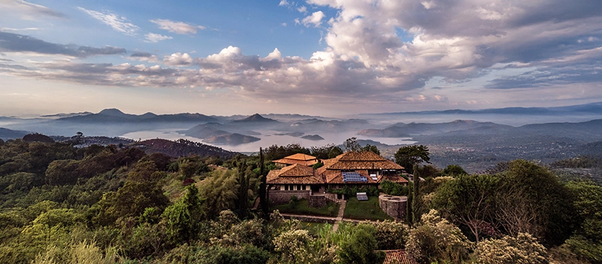 An elevated view of Virunga Lodge shows its stone cottages set above Lakes Bulera and Ruhondo, surrounded by forested hills and distant volcanoes.