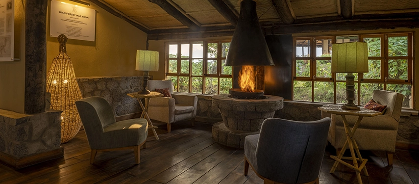 The main lounge at Virunga Lodge features a central fireplace, soft armchairs and wide windows framing the lush Rwandan countryside outside.