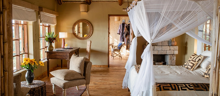 A spacious cottage interior at Virunga Lodge combines timber floors, handcrafted furnishings and a canopy bed, offering a warm retreat after gorilla trekking.