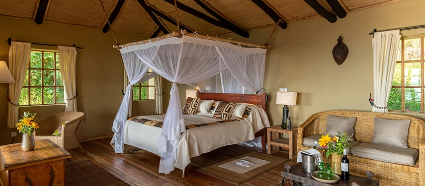 A beautifully appointed bedroom at Virunga Lodge features a canopy bed, woven furnishings and garden views that connect the space to its natural surroundings.