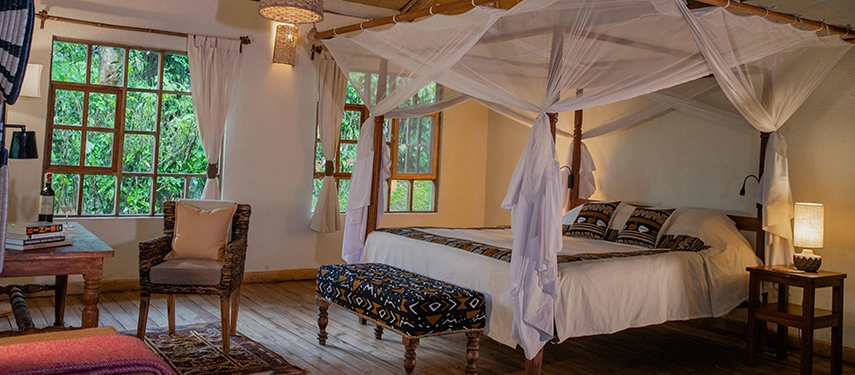 A light-filled bedroom at Volcanoes Bwindi Lodge with a four-poster bed, woven furnishings and views into the dense Bwindi forest.