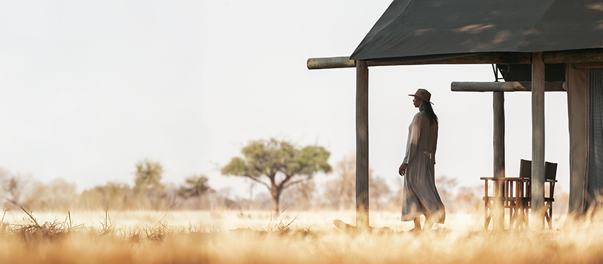 Guest in a wide-brimmed hat walking past her tent across golden grass