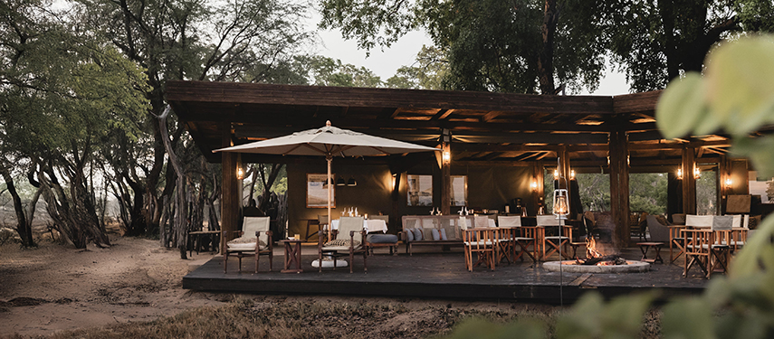 Cosy open-air lounge and dining deck with canvas roof at Davison’s Camp