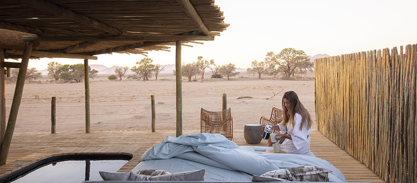 Guest enjoying a morning coffee in an open-air bed at Little Kulala Camp in Sossusvlei, Namibia