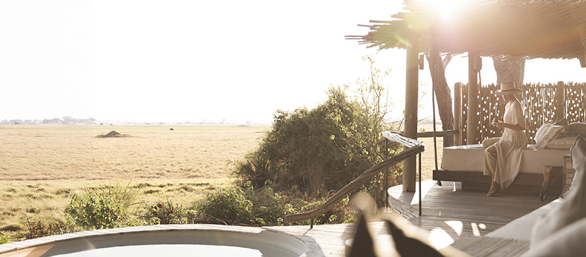 Woman looks out over the grassy plains of the Okavango Delta at sundown at a Little Mombo camp in Botswana