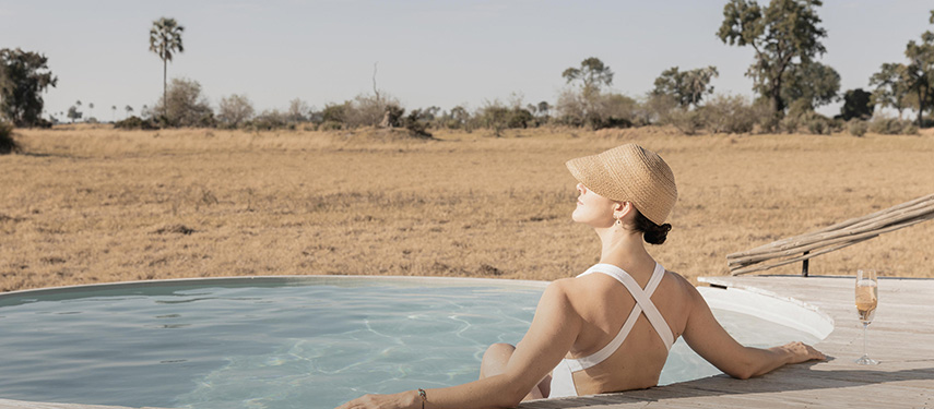 Woman looks out over the grassy plains of the Okavango Delta from a private plunge pool at a luxury safaro camp in Botswana