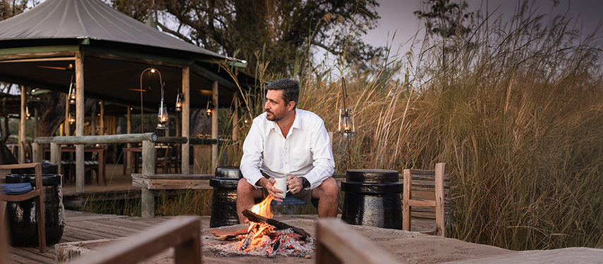 Man sits at a campfire at a luxury safari lodge in Botswana's Okavango Delta