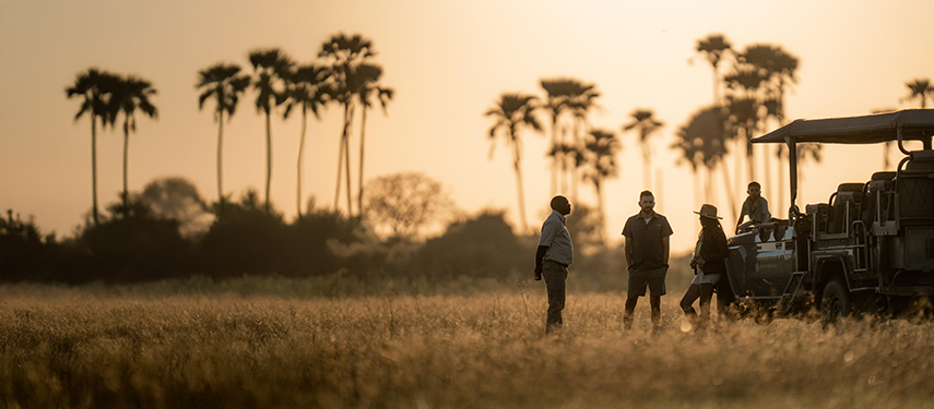 Guests and guide enjoy sundowners while on a game drive in Botswana