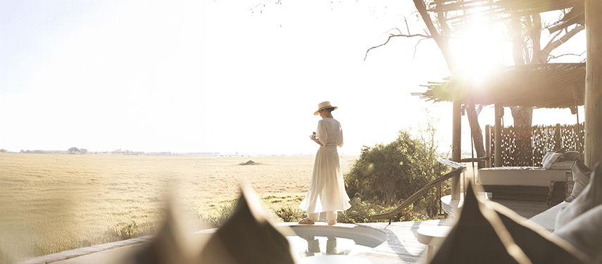 Beautiful image of lady dressed in white looking over the Botswana landscape at sunrise