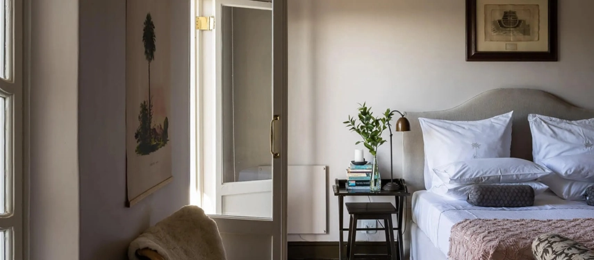 Elegant bedroom at Dorp Hotel with soft neutral tones, crisp white linens, and natural light streaming through French doors onto a private terrace.
