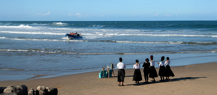 Staff welcoming guests arriving by boat on a pristine beach.