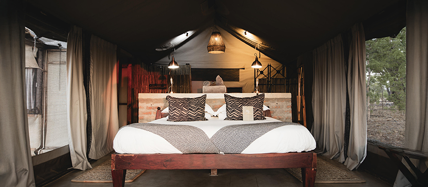 Interior of a canvas tent with a large bed and woven lampshades
