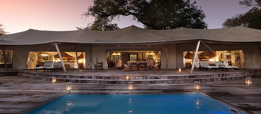 Exterior view of the Zarafa Dhow Suite in the Selinda Reserve at dusk, showing the expansive tented suite, wraparound deck and softly lit interiors.