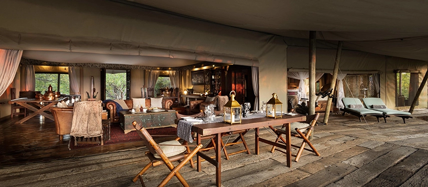 Open-plan living and dining area inside the Zarafa Dhow Suite in the Selinda Reserve, opening onto a wide timber deck with daybeds and bush views.