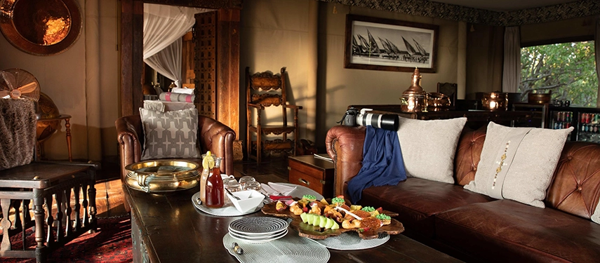 Detail of the Zarafa Dhow Suite lounge in the Selinda Reserve, showcasing leather sofas, curated antiques and a private in-suite dining spread.