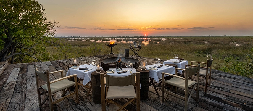 Sunset dinner setup at the Zarafa Dhow Suite in the Selinda Reserve, where an intimate table is positioned around a firepit with expansive wetland views.