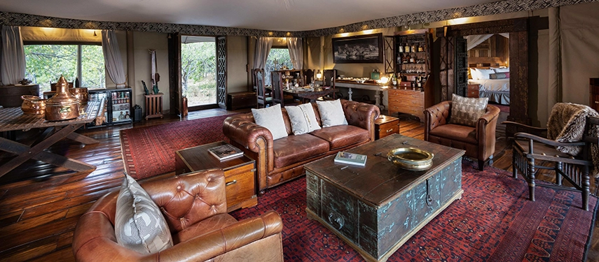 Spacious lounge area of the Zarafa Dhow Suite in the Selinda Reserve, styled with leather seating, Persian rugs and expansive bush-facing openings.