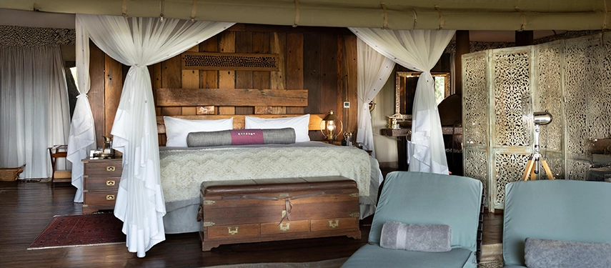Bedroom of the Zarafa Dhow Suite in the Selinda Reserve, featuring a four-poster bed, carved wooden details and sheer drapes opening onto the deck.