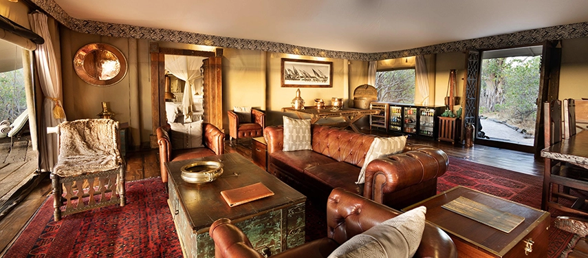 Elegant lounge inside the Zarafa Dhow Suite in the Selinda Reserve, featuring leather sofas, curated antiques and open views onto the surrounding wilderness.