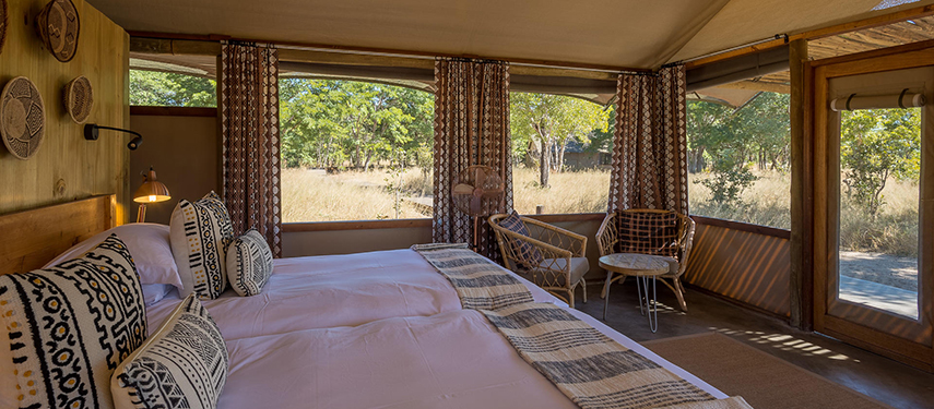 Interior of a canvas tent with twin beds, woven decor, and wide views of the bush.