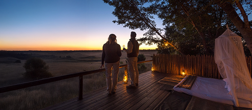 A couple enjoys sunset views from a lantern-lit star bed deck overlooking the plains.