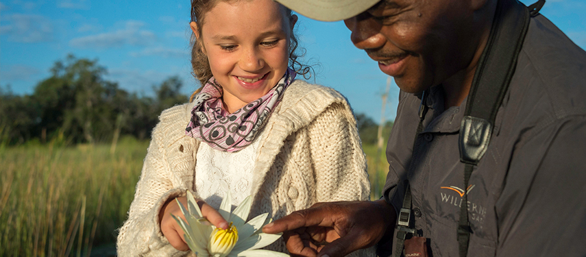 An African safari guide shows a young tourist a lily flower in Botswana's Okavango region